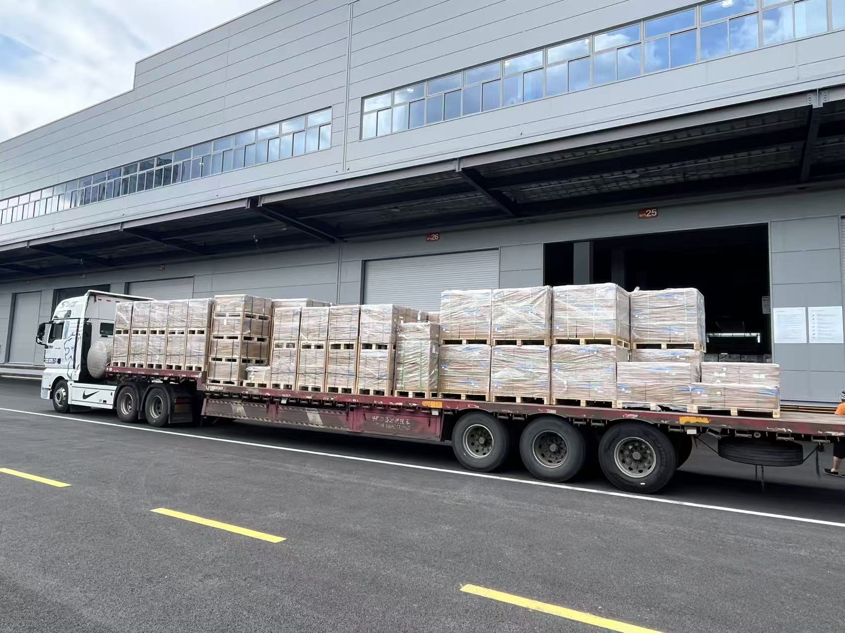 Full flatbed truck loaded with pallets of solar panels at warehouse dock